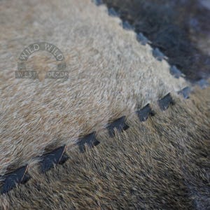 Close-up of a brown and gray cowhide rug with black stitching. The rug has a distressed look and is made of natural materials.