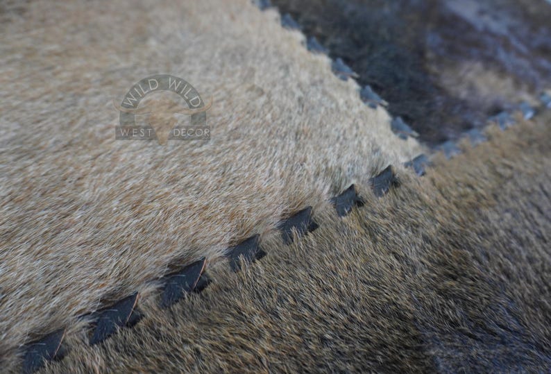 Close-up of a brown and gray cowhide rug with black stitching. The rug has a distressed look and is made of natural materials.