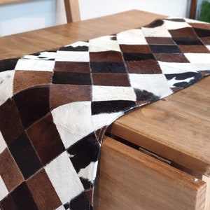 May include: A brown and white checkered table runner made of cowhide. The runner is on a wooden table.