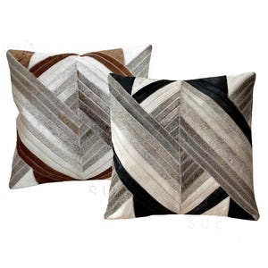 Könnte beinhalten: Zwei quadratische Kissen mit einem geometrischen Muster aus verschiedenen Brauntönen, Grau- und Weißtönen aus Leder. Die Kissen sind nebeneinander angeordnet.