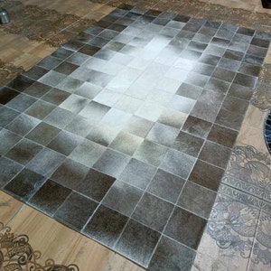 May include: A gray and white cowhide rug with a checkered pattern. The rug is made of natural cowhide and has a soft, luxurious feel.
