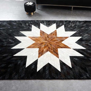 May include: A black, white and brown cowhide rug with a large star design in the centre. The rug is made of patchwork pieces of leather.