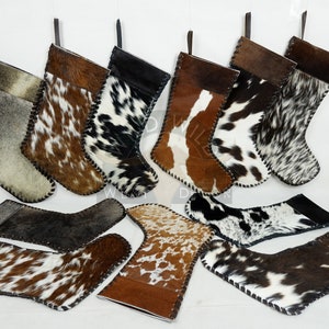 May include: A selection of Christmas stockings crafted from cowhide, showcasing diverse patterns of brown, black, and white fur. Each stocking includes a leather hanging loop and a stitched edge. Some stockings are displayed flat.
