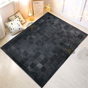 May include: Black and white cowhide patchwork rug with a square pattern. The rug has a black border and is made of real leather. The rug is on a light wood floor. The rug has the text "WILD WEST DECOR" on it.