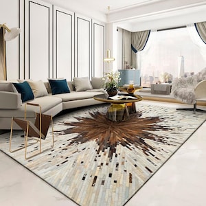 Puede incluir: Una sala de estar moderna con un sofá seccional blanco, una alfombra de cuero marrón y piel de vaca blanca y una mesa de café de vidrio con base dorada. La alfombra tiene un patrón de estrella.