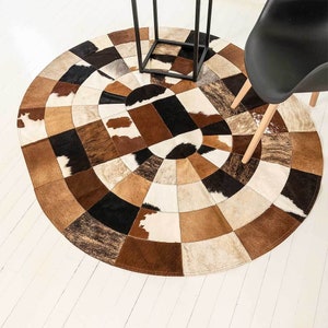 May include: A round, multi-coloured cowhide rug with a patchwork design. The rug is made of different shades of brown, black, and white cowhide.