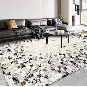 Puede incluir: Un sofá de cuero negro con una alfombra de patchwork blanco y negro. La alfombra tiene un patrón de cuadros y está hecha de piel de vaca.
