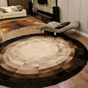 Puede incluir: Una alfombra grande, redonda y multicolor hecha de piezas de cuero. La alfombra tiene un patrón circular en el centro y un borde marrón oscuro.
