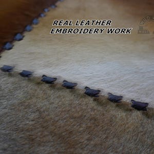 Close-up of a brown, white, and tan leather patchwork rug with black stitching.