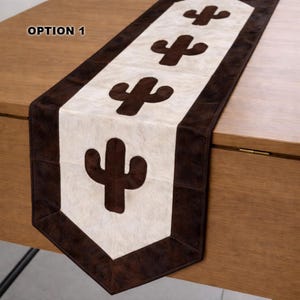 May include: A rectangular table runner with a brown and white cactus design. The runner has a white center with brown cactus shapes and a brown border. The text "OPTION 1" is in the upper left corner.