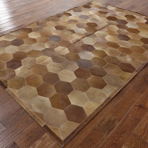May include: A brown and beige cowhide rug with a hexagonal pattern. The rug is made of natural leather and has a rustic look.