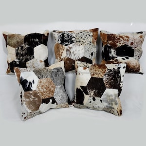 May include: Five decorative throw pillows with a patchwork design. The pillows feature a cowhide pattern in shades of brown, black, white, and tan. The geometric shapes create a unique and rustic aesthetic. These pillows are perfect for adding texture and visual interest to any living space.
