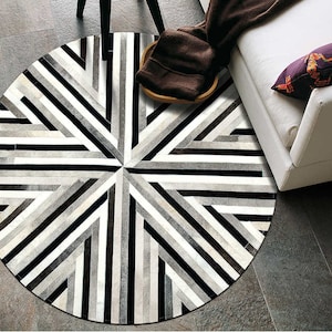 May include: A round, black and white striped rug with a geometric pattern. The rug is made of cowhide and has a modern design.