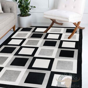 May include: Black and white cowhide rug with a geometric pattern of squares. The rug has a black border and a logo that says "Wild West Decor".