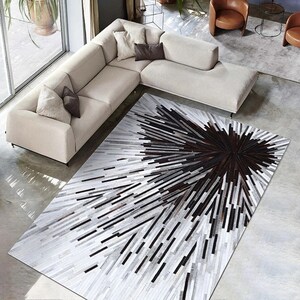 Pu&ograve; includere: Un tappeto in pelle di mucca bianco e nero con un motivo geometrico. Il tappeto ha un centro marrone scuro con linee radianti di pelle bianca e nera.