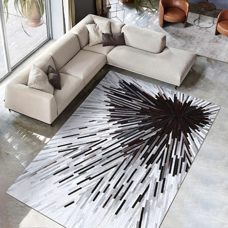 Pu&ograve; includere: Un tappeto in pelle di mucca bianco e nero con un motivo geometrico. Il tappeto ha un centro marrone scuro con linee radianti di pelle bianca e nera.