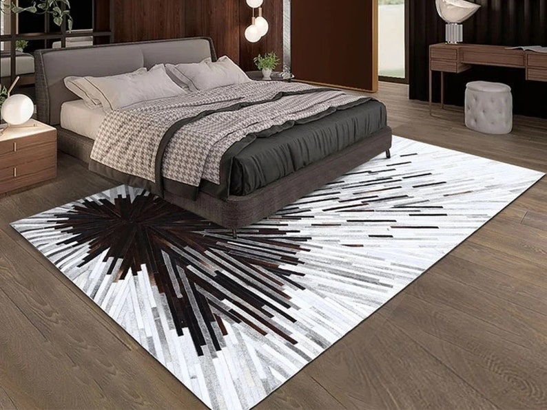Pu&ograve; includere: Un tappeto in pelle di mucca bianco e nero con un motivo geometrico. Il tappeto &egrave; posizionato in una camera da letto con un letto e un comodino.