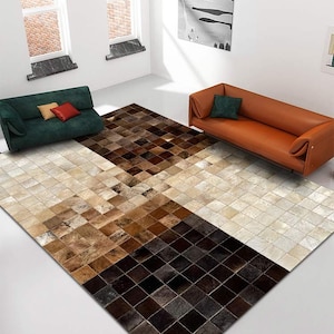 Puede incluir: Una alfombra de piel de vaca patchwork marrón, blanco y negro con un patrón cuadrado. La alfombra se coloca en un salón con un sofá verde y un sofá naranja.