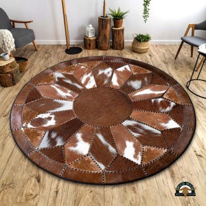 May include: A round brown and white cowhide patchwork rug with a circular design. The rug is made of different pieces of cowhide sewn together to create a unique pattern. The rug is perfect for adding a touch of rustic charm to any room.