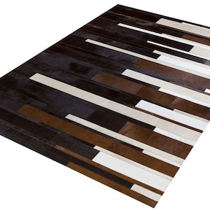 Peut inclure: Un tapis en patchwork brun, noir et blanc avec un motif géométrique. Le tapis est en cuir et a un design moderne.