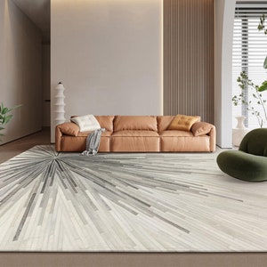 Pu&ograve; includere: Un soggiorno moderno con un divano in pelle marrone e un tappeto geometrico grigio e bianco. Il tappeto ha un motivo a stella con uno sfondo bianco e linee grigie che si irradiano verso l'esterno.