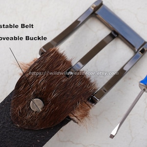May include: A close-up of a black belt with a removable buckle and a brown fur accent. A blue and silver screwdriver is next to the belt. The text "Adjustable Belt" and "Removable Buckle" are visible.
