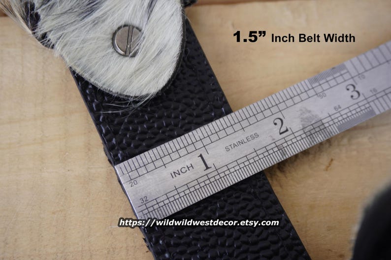 May include: Close-up of a black leather belt with a textured surface, featuring a buckle with a white and gray fur accent. The belt width is 1.5 inches. The Etsy shop URL is visible at the bottom.