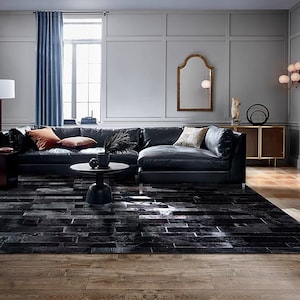 May include: A large black leather sectional sofa with cushions in a living room featuring a black and white cowhide rug, a wooden coffee table, and a gold mirror.