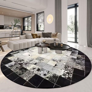 May include: A black and white cowhide rug with a geometric pattern. The rug is round and has a black border. The rug is in a living room with a white sofa and two coffee tables.