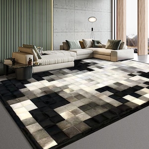 May include: A black and white patchwork rug made of cowhide. The rug is laid out in a living room with a modern sectional sofa.