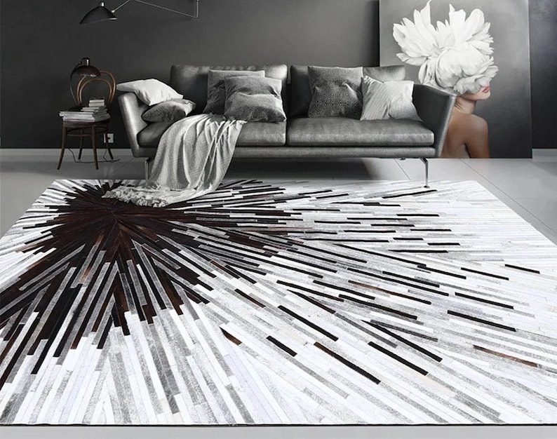 Pu&ograve; includere: Un tappeto in pelle di mucca bianco e nero con un motivo geometrico. Il tappeto ha un grande cerchio marrone scuro al centro.