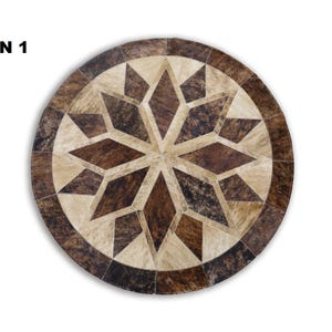 Puede incluir: Alfombra redonda de piel de vaca con diseño de estrella. La alfombra presenta un diseño central de estrella en tonos marrón y beige, rodeado por un borde marrón oscuro. La alfombra está hecha de piel de vaca natural.