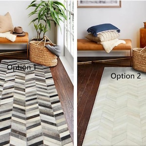 May include: Two options for a cowhide rug in a chevron pattern. Option 1 is a multi-colored rug with shades of gray, white, and black. Option 2 is a white rug with a subtle gray pattern.