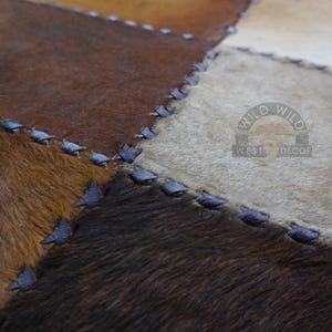 A patchwork rug made of different colored cowhide pieces, stitched together with dark blue thread. The rug has a light brown, dark brown, and white color scheme.