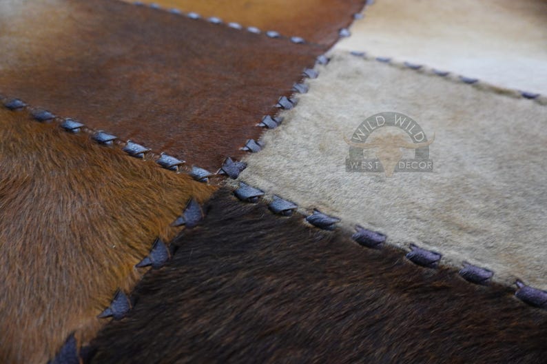 A patchwork rug made of different colored cowhide pieces, stitched together with dark blue thread. The rug has a light brown, dark brown, and white color scheme.