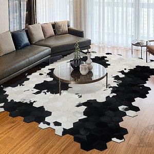 May include: A black and white cowhide rug with a hexagonal pattern. The rug is in a living room setting with a leather sofa, a coffee table, and a chair.