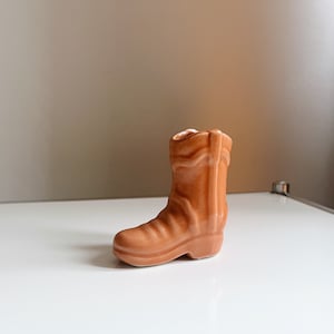 Könnte beinhalten: Ein kleiner, brauner Keramik-Pflanztopf in Form eines Stiefels. Der Stiefel ist schlicht gehalten mit abgerundeter Spitze und einem leichten Absatz.