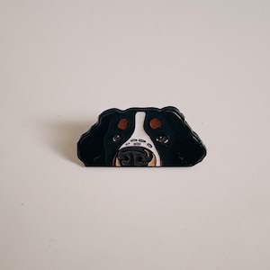Könnte beinhalten: Dekoratives Objekt in Form eines Hundegesichts, schwarz, weiß und braun. Der Hund hat braune Augen, eine schwarze Nase und einen weißen Streifen im Gesicht. Die Ohren sind schwarz, und das Design ist cartoonartig.
