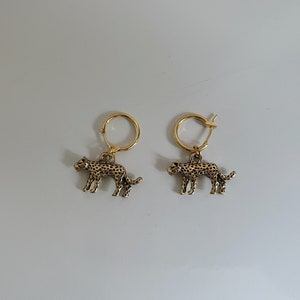 May include: A pair of gold hoop earrings with a leopard charm hanging from each hoop.