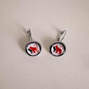Può includere: Un paio di orecchini d'argento con sfondo bianco e un logo animale rosso e nero. Il logo dice "Animal Justice Action".