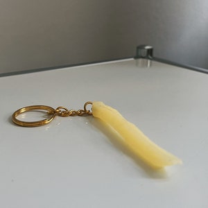 Könnte beinhalten: Ein goldener Schlüsselanhänger mit einem gelben Gummifritten-Anhänger.