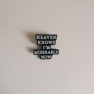 Puede incluir: Pin de esmalte negro con texto blanco que dice "Heaven Knows I'm Miserable Now".