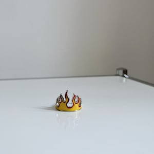 Könnte beinhalten: Ein silberner Ring mit einem Flammen-Design aus gelbem und rotem Email.