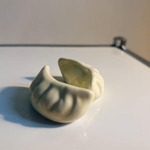 Könnte beinhalten: Zwei weiße Keramik-Knödel, einer leicht geöffnet, auf einer weißen Oberfläche.