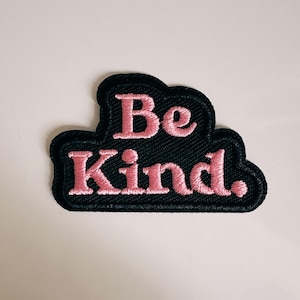 Op de afbeelding: Een zwart geborduurd embleem met de woorden "Be Kind" in roze script. De patch heeft een wolkvorm en is ontworpen om op kleding of accessoires te worden genaaid of gestreken.