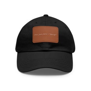 Könnte beinhalten: Eine schwarze Baseballkappe mit einem rechteckigen braunen Aufnäher in der Mitte der Vorderseite. Der Aufnäher zeigt den weißen Text your_text_here = "design" in einer Schreibmaschinenschrift. Die Kappe hat einen gebogenen Schirm und Ösen.