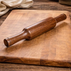 May include: A wooden rolling pin with a dark brown finish rests on a wooden cutting board. The rolling pin is cylindrical with rounded handles on each end. The cutting board is rectangular and also made of wood, with a lighter brown color.