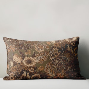 Puede incluir: Una almohada rectangular con un estampado floral en tonos marrones, beige y verde oliva. El diseño presenta flores, hojas y pájaros detallados, creando una estética vintage. Un accesorio decorativo para el hogar.