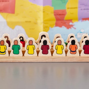 May include: A row of wooden figures, each painted a different color, standing in a line on a wooden base. The figures are all facing the same direction and have a simple, cartoon-like design.