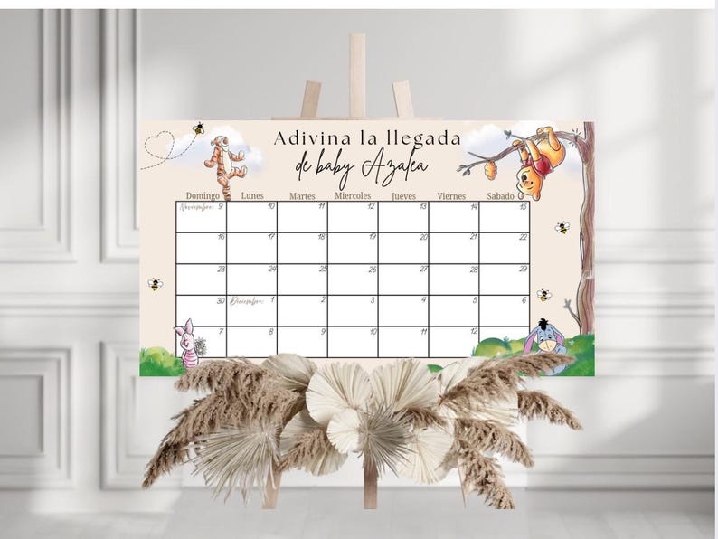 May include: A baby shower calendar with Winnie the Pooh characters. The calendar has a beige background with a grid for dates and the text "Adivina la llegada de baby Azalea". Decorative elements include bees, clouds, and floral accents.